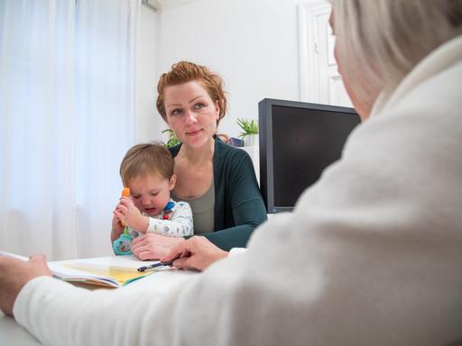 Symbolbild: Mutter mit Kind mit Ärztin im Sprechzimmer