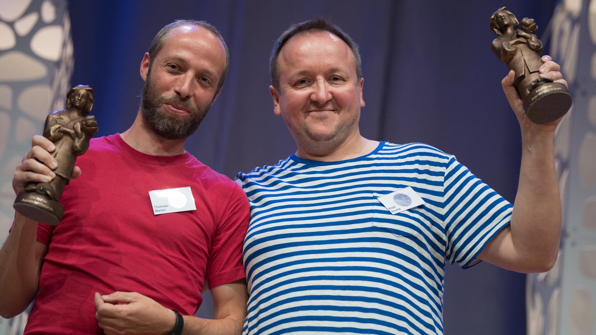 Der polnische Autor und Illustrator Pjotr Socha (r) und der Übersetzer Thomas Weiler halten bei der Verleihung des Deutschen Jugendliteraturpreises 2017 auf der Buchmesse in Frankfurt am Main (Hessen) ihre Momo-Trophäen hoch. Der polnische Autor und Illustrator Pjotr Socha (r) und der Übersetzer Thomas Weiler halten bei der Verleihung des Deutschen Jugendliteraturpreises 2017 auf der Buchmesse in Frankfurt am Main (Hessen) ihre Momo-Trophäen hoch.