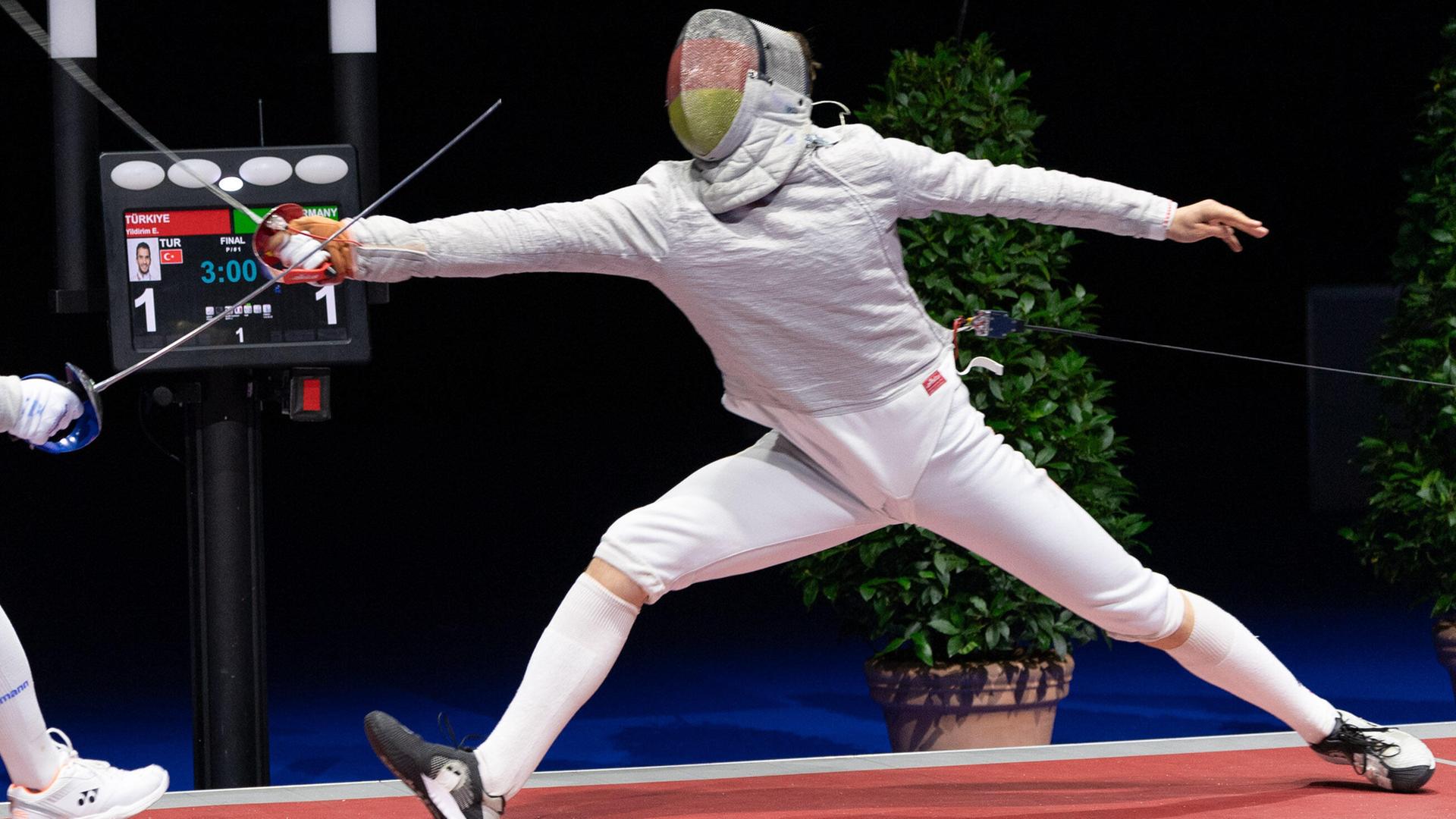 In weißem Fechtanzug gekleideter Mann mit einem Säbel im Ausfallschritt. In weißem Fechtanzug gekleideter Mann mit einem Säbel im Ausfallschritt.