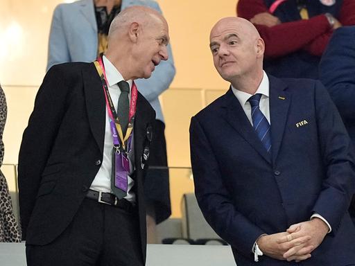 Bernd Neuendorf steht auf einer Stadiontribüne neben Gianni Infantino und spricht mit ihm.