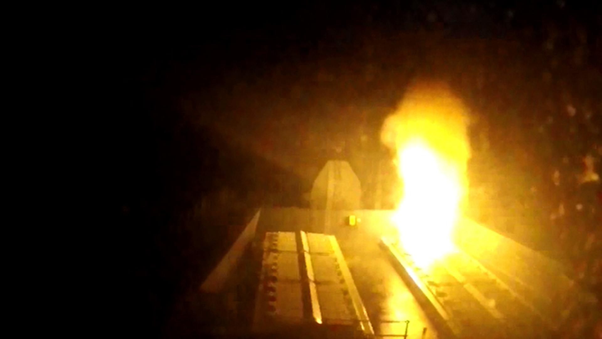 Es ist dunkel. Man sieht sehr unscharf das Feuer aus der Rakete aus dem Deck des Schiffen hochsteigen, das dadurch erhellt wird.