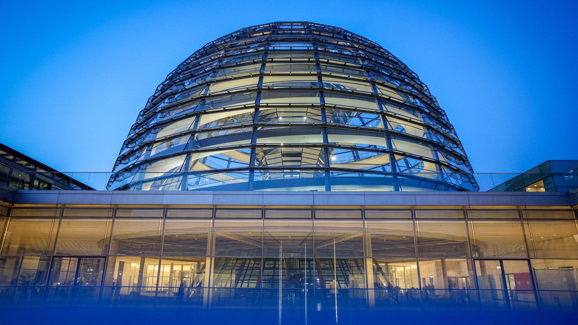 Blick auf die gäserne Reichstagskuppel des Bundestags mit blauem Hintergrund.  