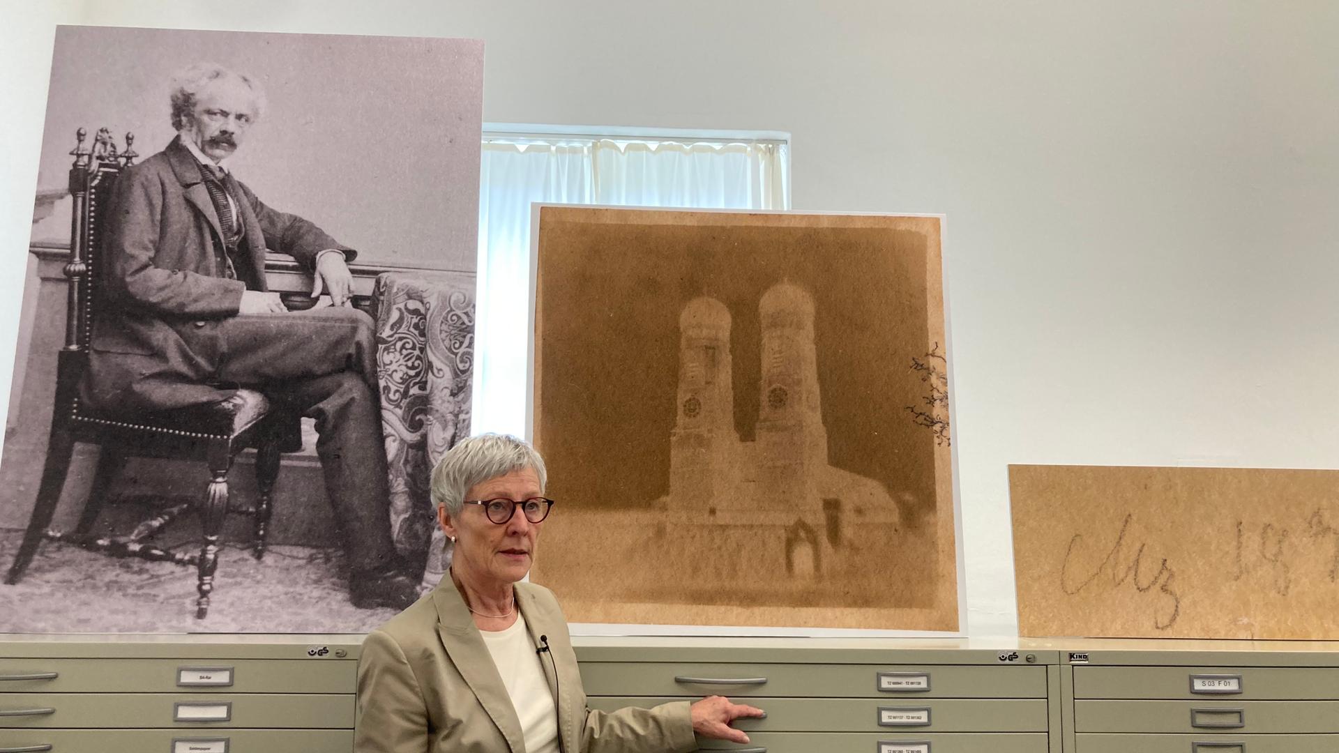 Die Wissenschaftlerin Cornelia Kemp steht vor einem Schrank. Auf dem Schrank steht ein großes, gelbliches Foto. Es zeigt die Münchner Frauenkirche.