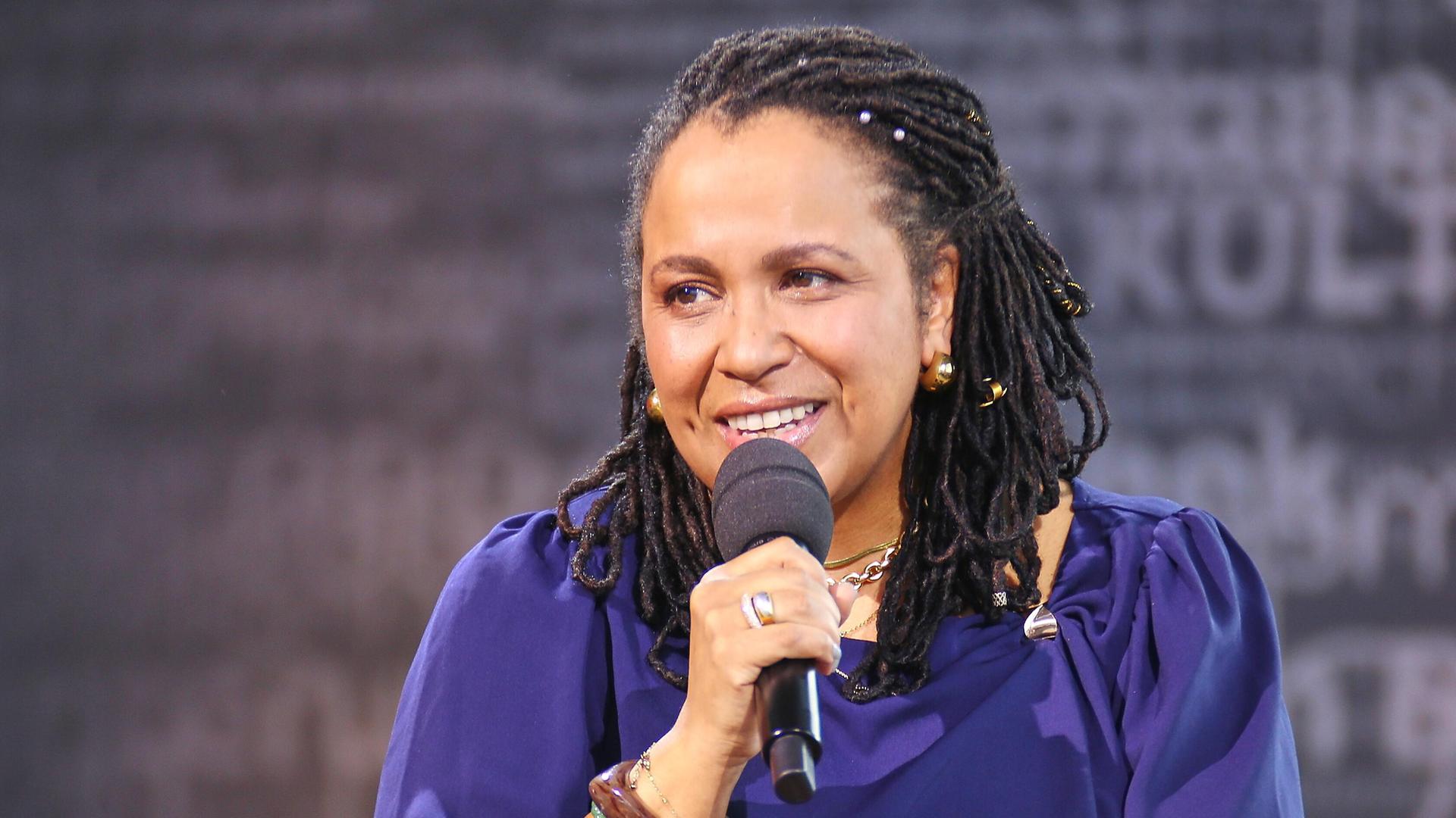 Die Antirassismus-Trainerin Tupoka Ogette hält während eines Interviews ein Mikrofon. Sie trägt ein lilafarbenes Oberteil und guckt in Richtung des Interviewenden.