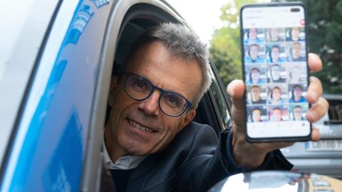 Uwe Baltner sitzt in seinem Auto und zeigt auf seinem Handy sein Instagram-Profil. 