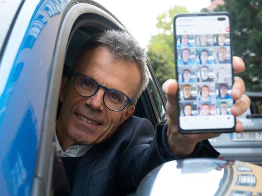 Uwe Baltner sitzt in seinem Auto und zeigt auf seinem Handy sein Instagram-Profil. 
