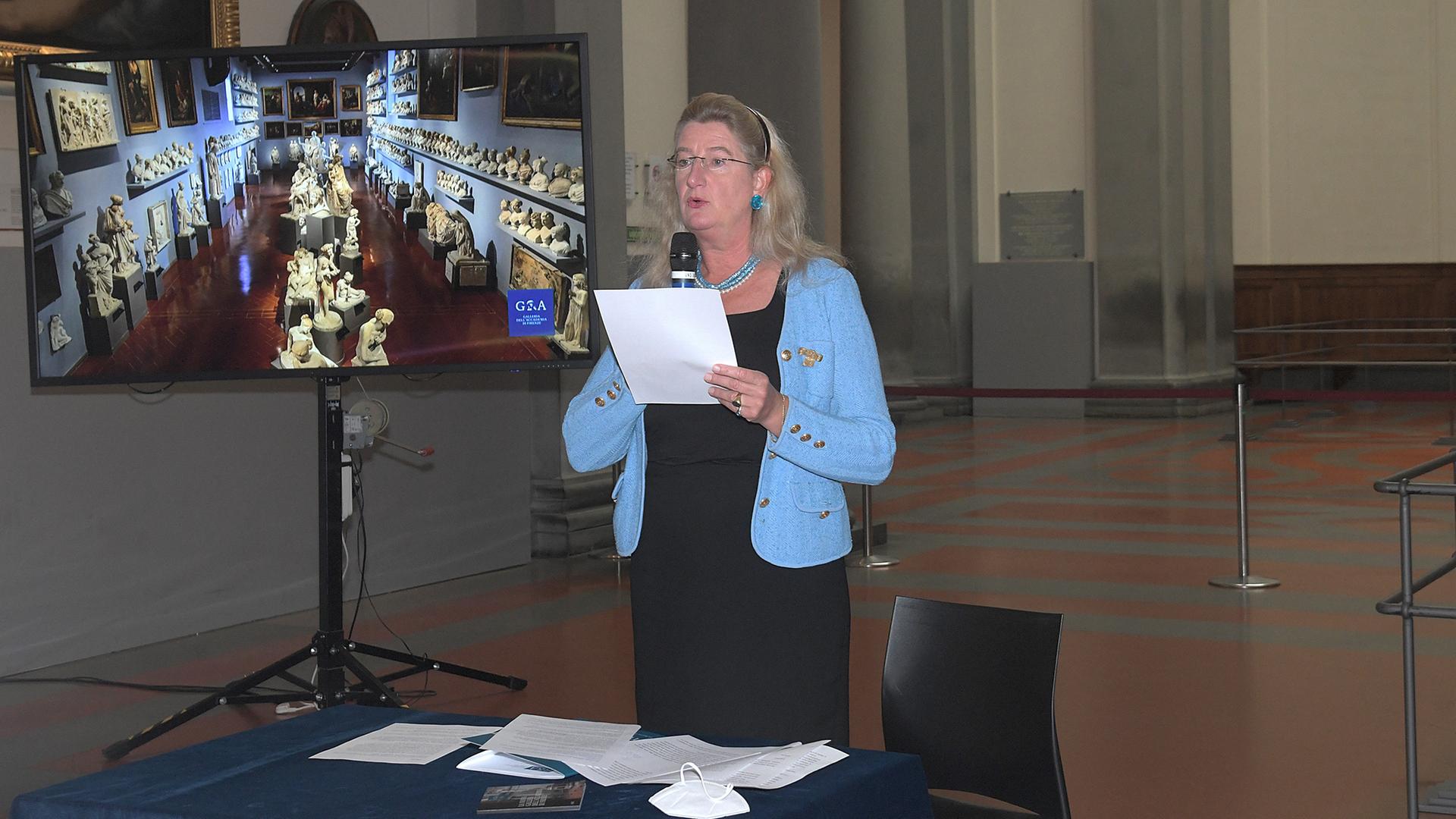 Die Direktorin des Kunstmuseums Galleria dell'Accademia in Florenz, Cecilie Hollberg, steht hinter einem Schreibtisch, hält ein Dokument in den Händen und spricht in ein Mikrofon. Hinter ihr ein Bildschirm mit Blick in das Museum. Die Direktorin des Kunstmuseums Galleria dell'Accademia in Florenz, Cecilie Hollberg, steht hinter einem Schreibtisch, hält ein Dokument in den Händen und spricht in ein Mikrofon. Hinter ihr ein Bildschirm mit Blick in das Museum.