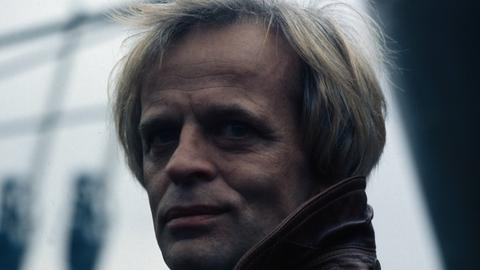 Der deutsche Schauspieler Klaus Kinski im Hafen von Hamburg. Der damalige Endvierziger trägt eine Lederjacke. Er hat blonde Haare.