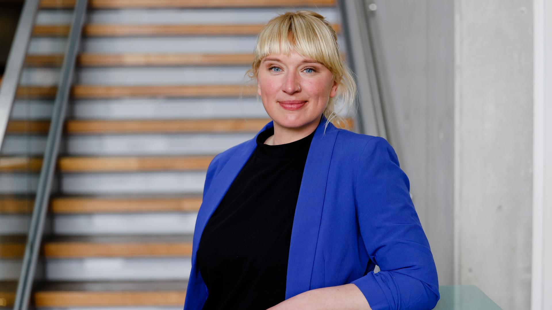 Eine Frau steht vor einer Treppe und schaut lächelnd in die Kamera Eine Frau steht vor einer Treppe und schaut lächelnd in die Kamera