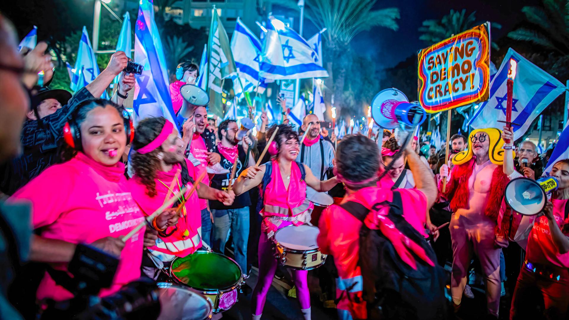 Demonstrierende mit israelischen Flaggen, Trommeln und Trillerpfeifen nachts in Tel Aviv.