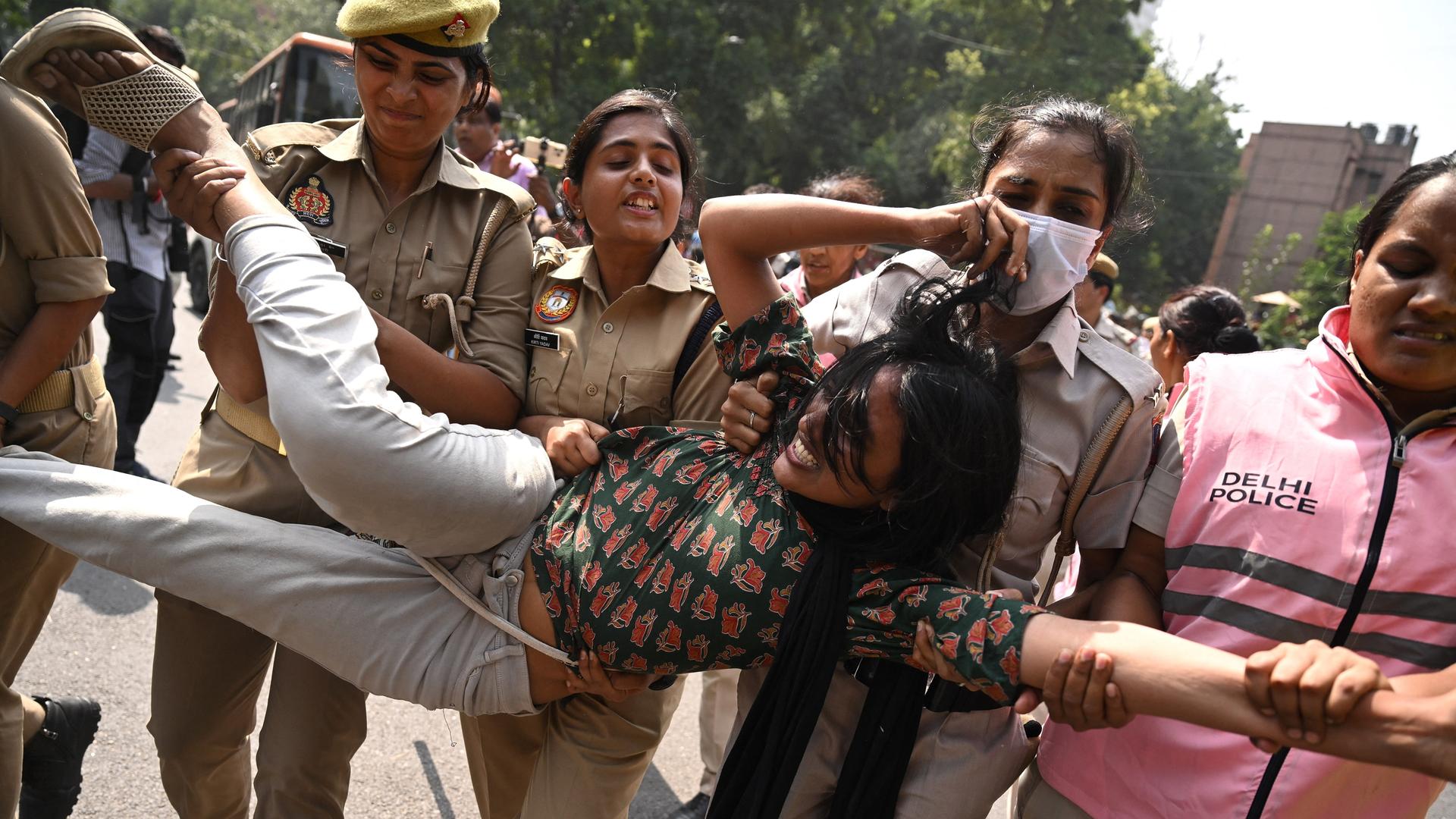 Polizeikräfte nehmen in Neu-Delhi eine Anhängerin der „Cockroach Janata Party“ (CJP) fest. Die Demonstrantin wird von mehreren uniformierten Polizistinnen getragen.