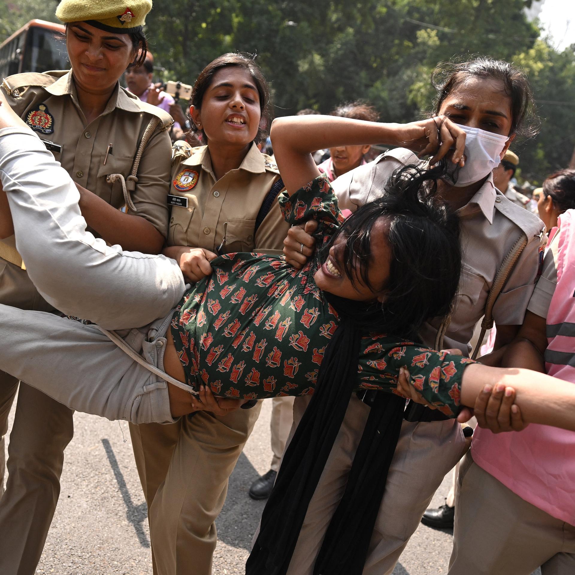 Polizeikräfte nehmen in Neu-Delhi eine Anhängerin der „Cockroach Janata Party“ (CJP) fest. Die Demonstrantin wird von mehreren uniformierten Polizistinnen getragen.