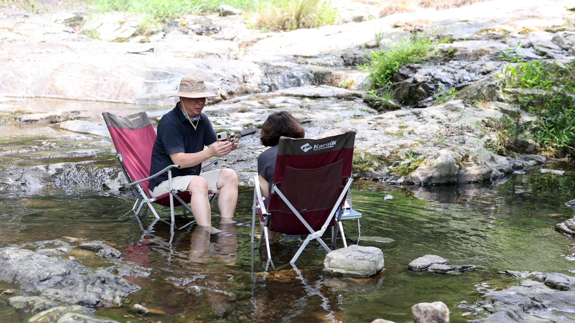 Ein Paar sitzt auf Campingstühlen mit den Füßen in einem Fluß. Ein Paar sitzt auf Campingstühlen mit den Füßen in einem Fluß.