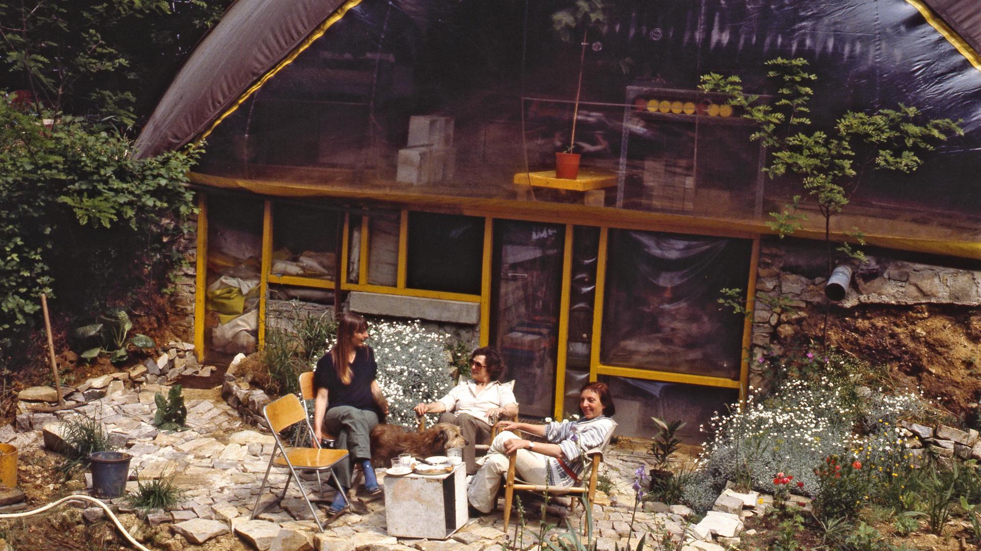 Drei Personen sitzen im Wald vor einem aufblasbaren Haus.