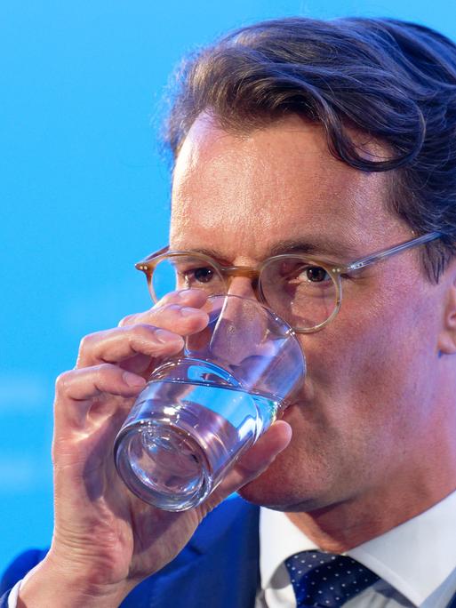 Hendrik Wüst, Ministerpräsident von Nordrhein-Westfalen, trinkt vor einem blauen Hintergrund ein Glas Wasser.