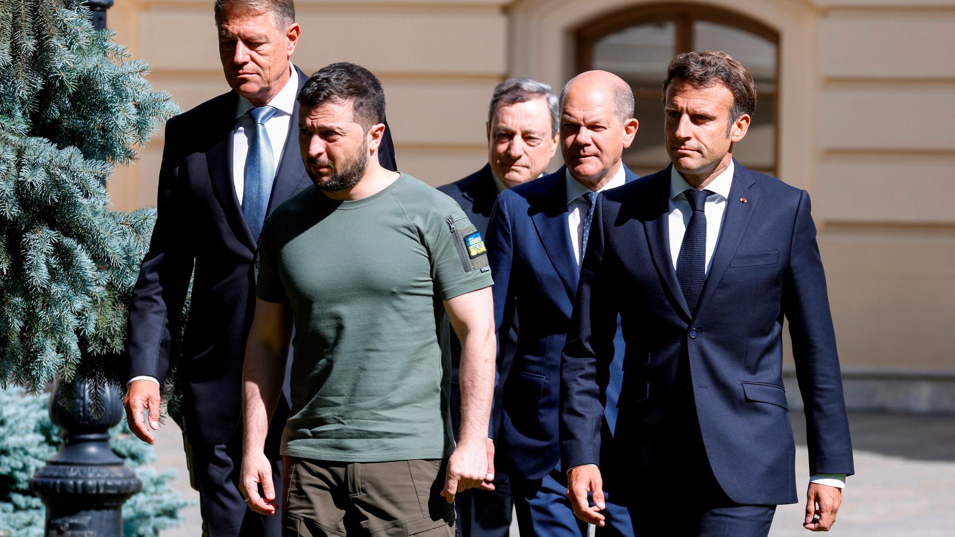 Frankreichs Präsident Emmanuel Macron, der rumänische Präsident Klaus Johannis, Italiens Premierminister Mario Draghi und Bundeskanzler Olaf Scholz, alle in Anzug, stehen mit Präsident Wolodimir Selenski, in Militärkleidung, zusammen.