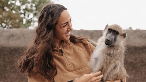 Aufnahme zeigt eine junge Frau (Primatologin Michi Schreiber) mit einem Affen auf dem Arm beim Bushwalk in Simbabwe 2024
Aufnahme zeigt eine junge Frau (Primatologin Michi Schreiber) mit einem Affen auf dem Arm beim Bushwalk in Simbabwe 2024