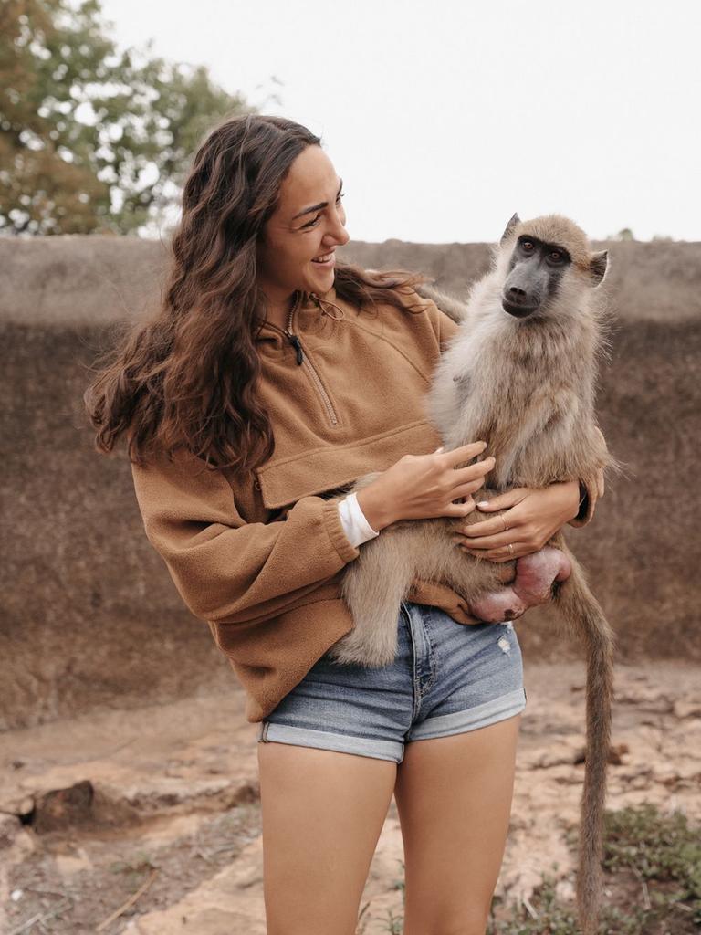 Aufnahme zeigt eine junge Frau (Primatologin Michi Schreiber) mit einem Affen auf dem Arm beim Bushwalk in Simbabwe 2024
