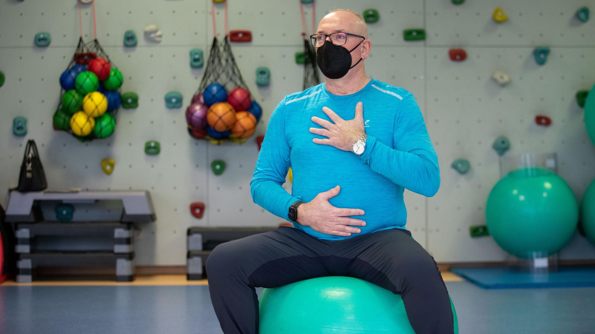 Ein Patient balanciert auf einem Sitzball und hat die Hände für eine Atemübung auf Brustkorb und Bauch gelegt.