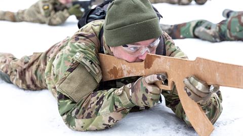 Ukrainische Zivilisten trainieren den Umgang mit der Waffe. Sie tragen Tarnanzüge und liegen im Schnee. Im Bildvordergrund hält ein Mann eine Waffenattrappe im Anschlag.