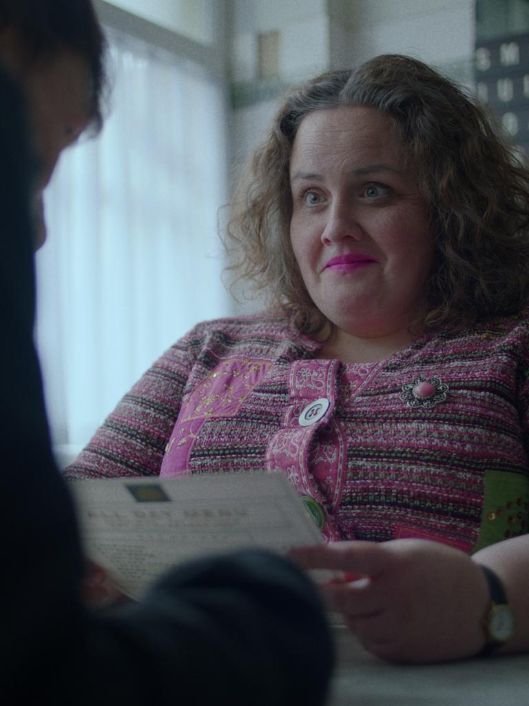 Szene aus der Serie "Rentierbaby": Eine lächelnde Frau (Jessica Gunning) sitzt an einem Schreibtisch einer anderen Person gegenüber und hält einen Brief in der Hand. 