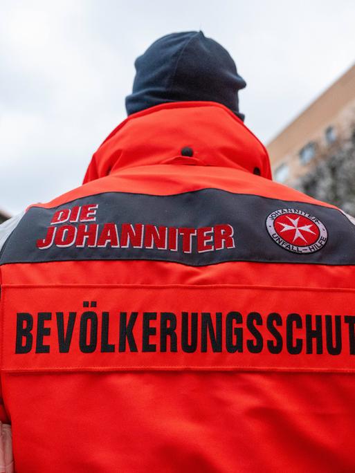 Ein Mann mit roter Jacke, auf deren Rückseite die Aufschrift "Die Johanniter - Bevölkerungsschutz" zu lesen ist