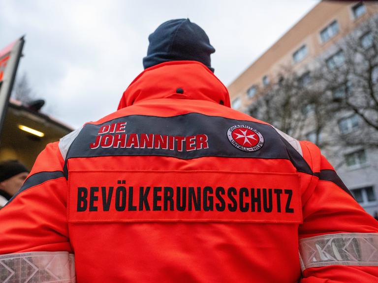 Ein Mann mit roter Jacke, auf deren Rückseite die Aufschrift "Die Johanniter - Bevölkerungsschutz" zu lesen ist