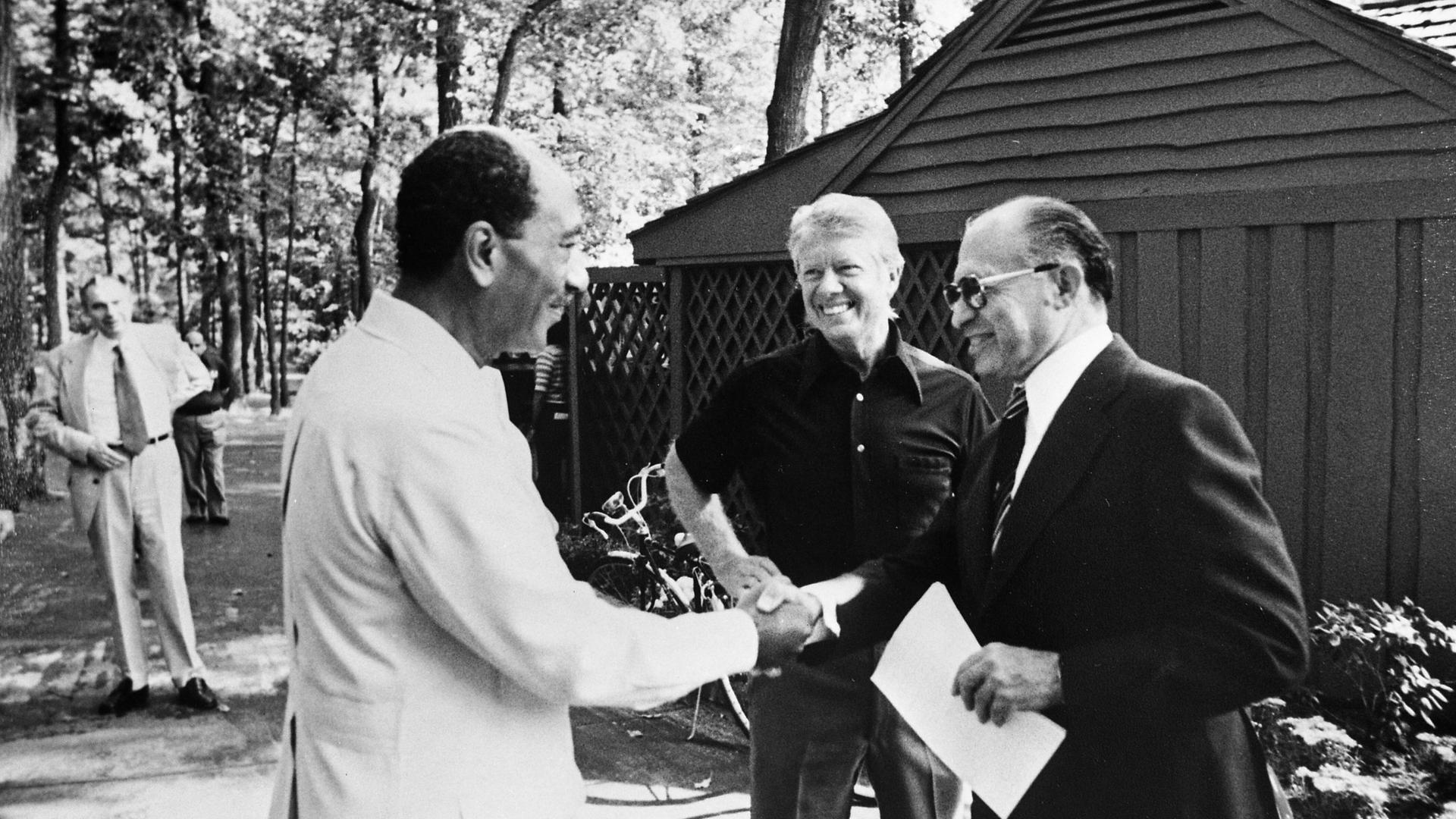Ein historisches Schwarzweiß-Foto  von 1979 zeigt den israelischen Ministerpräsidenten Menachem Begin mit dem ägyptischen Staatspräsidenten Anwar as Sadat beim Handschlag. In der Mitte steht der damalige US-Präsident Jimmy Carter.