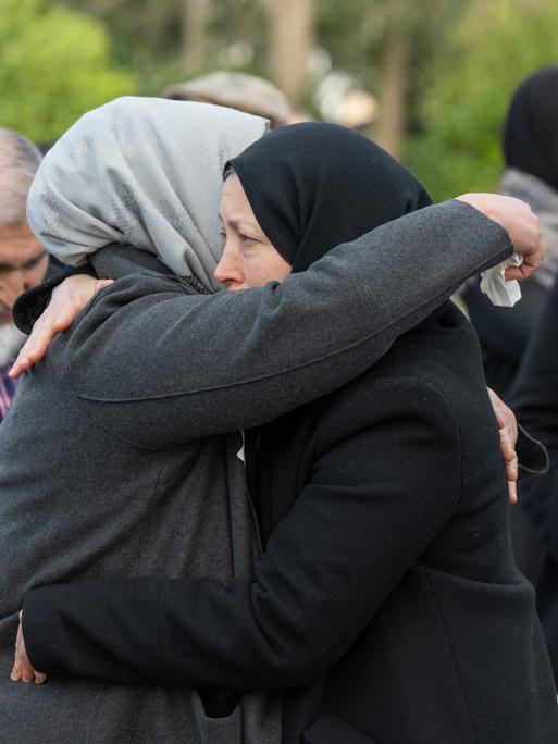 Zwei Frauen umarmen sich beim Gedenken an ihre ermordeten Angehörigen auf einem Friedhof
