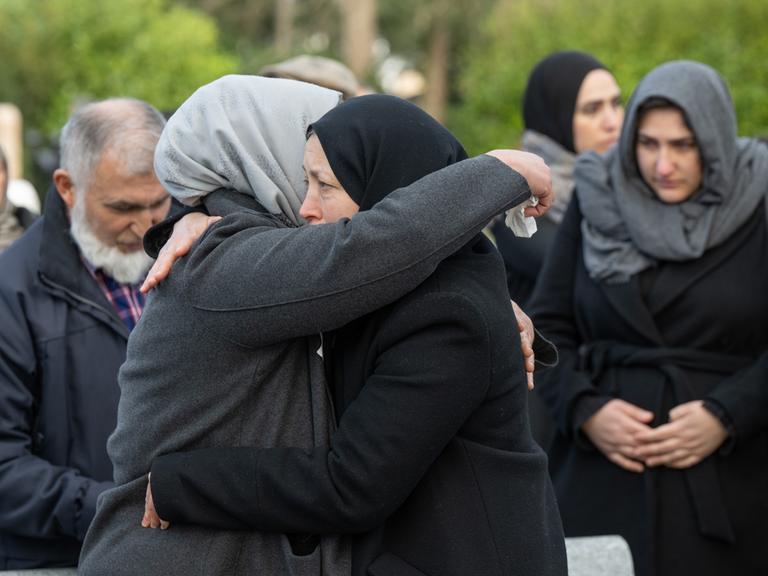 Zwei Frauen umarmen sich beim Gedenken an ihre ermordeten Angehörigen auf einem Friedhof