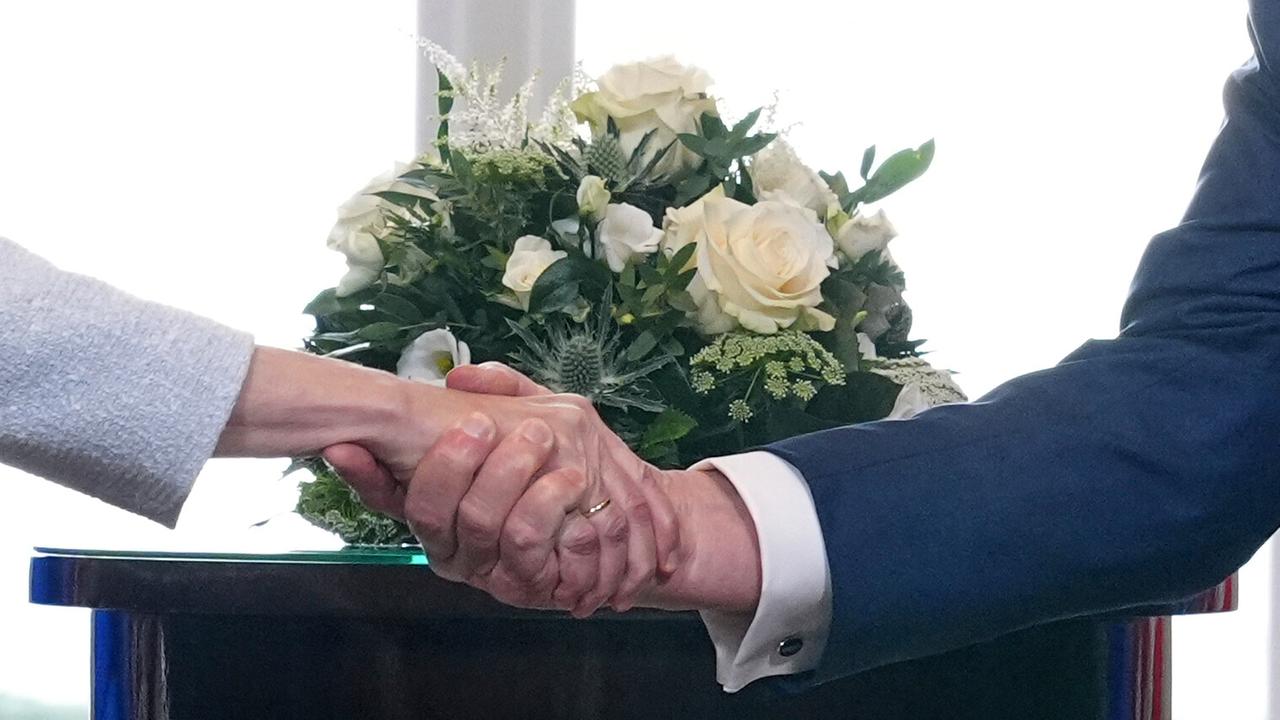 Handschlag einer Frau (Ursula von der Leyen) mit einem Mann (Donald Trump) vor einem Blumenstrauß mit weißen Rosen.