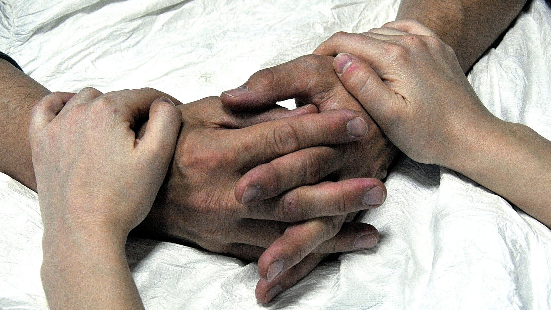 Hände eines älteren und eines jüngeren Menschen auf einer Bettdecke