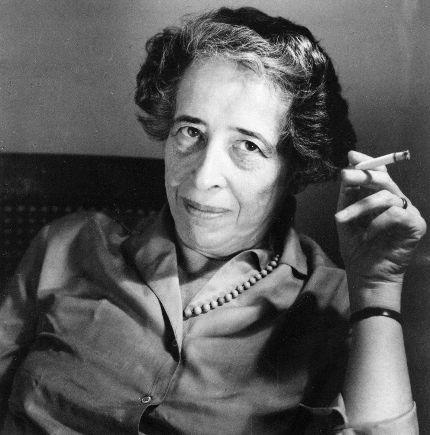 Die Schwarz-Weiß-Fotografie zeigt die Philosophin Hannah Arendt (1906-1975) mit einer Zigarette in der Hand. Sie blickt den Betrachter direkt an.