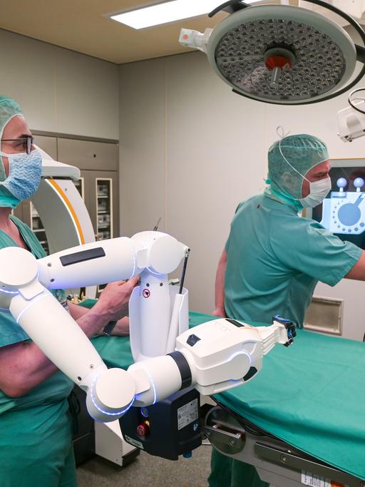 Zwei Ärzte verfolgen auf dem Bildschirm die OP, welche durch einen Roboter unterstützt wird.
