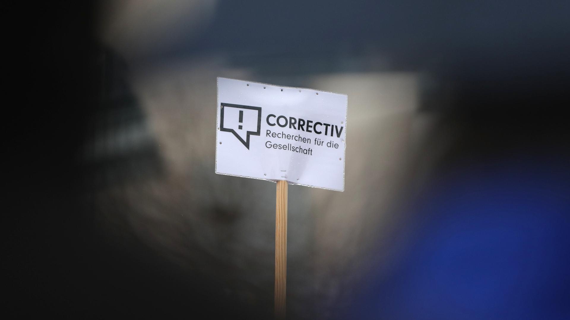Schild mit dem Logo des Medienkollektivs "Correctiv" und der Aufschrift "Correctiv-Recherchen für die Gesellschaft" vor einem verschwommenem Hintergrund