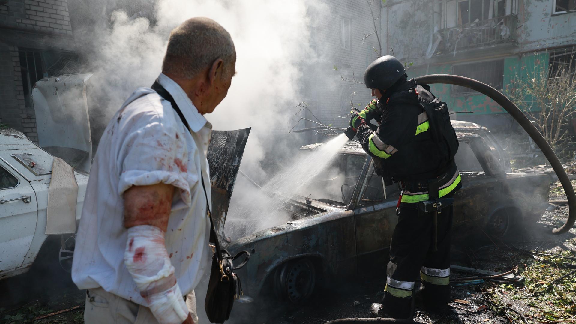 In der ukrainischen Stadt Saporischschja löscht ein Feuerwehrmann in Anwesenheit eines verletzten Anwohners ein brennendes Auto. In der ukrainischen Stadt Saporischschja löscht ein Feuerwehrmann in Anwesenheit eines verletzten Anwohners ein brennendes Auto.