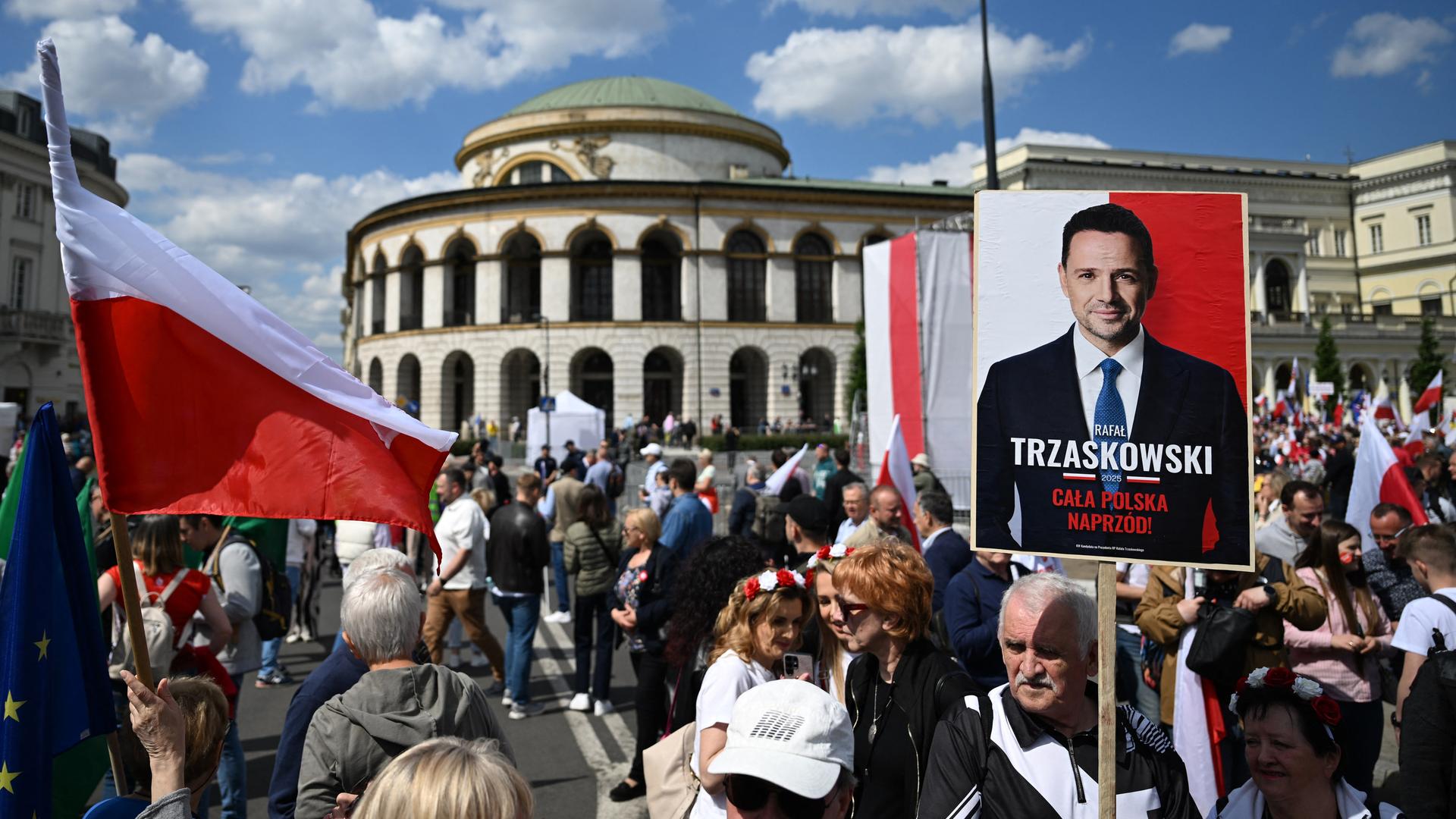 Eine Menschenmenge in der Innenstadt von Warschau schwernkt Flaggen in den Landesfarben rot und weiß und hält ein Plakat mit dem Bild des Präsidentschaftskandidaten Trzaskowski hoch