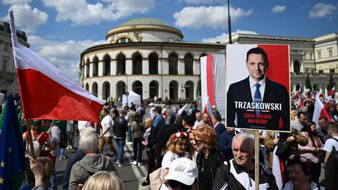 Eine Menschenmenge in der Innenstadt von Warschau schwernkt Flaggen in den Landesfarben rot und weiß und hält ein Plakat mit dem Bild des Präsidentschaftskandidaten Trzaskowski hoch