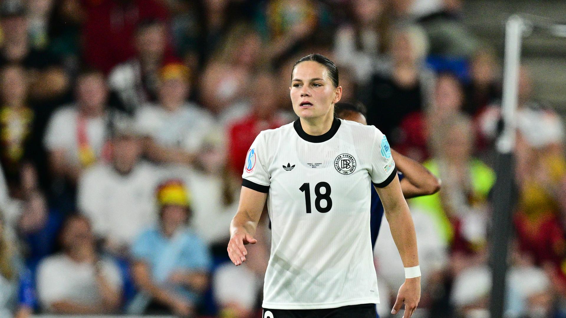 Giovanna Hoffmann trägt das Trikot des deutschen Nationalteams und geht über den Fußballplatz. Im Hintergrund sind schemenhaft Zuschauer auf den Rängen zu sehen. Giovanna Hoffmann trägt das Trikot des deutschen Nationalteams und geht über den Fußballplatz. Im Hintergrund sind schemenhaft Zuschauer auf den Rängen zu sehen.
