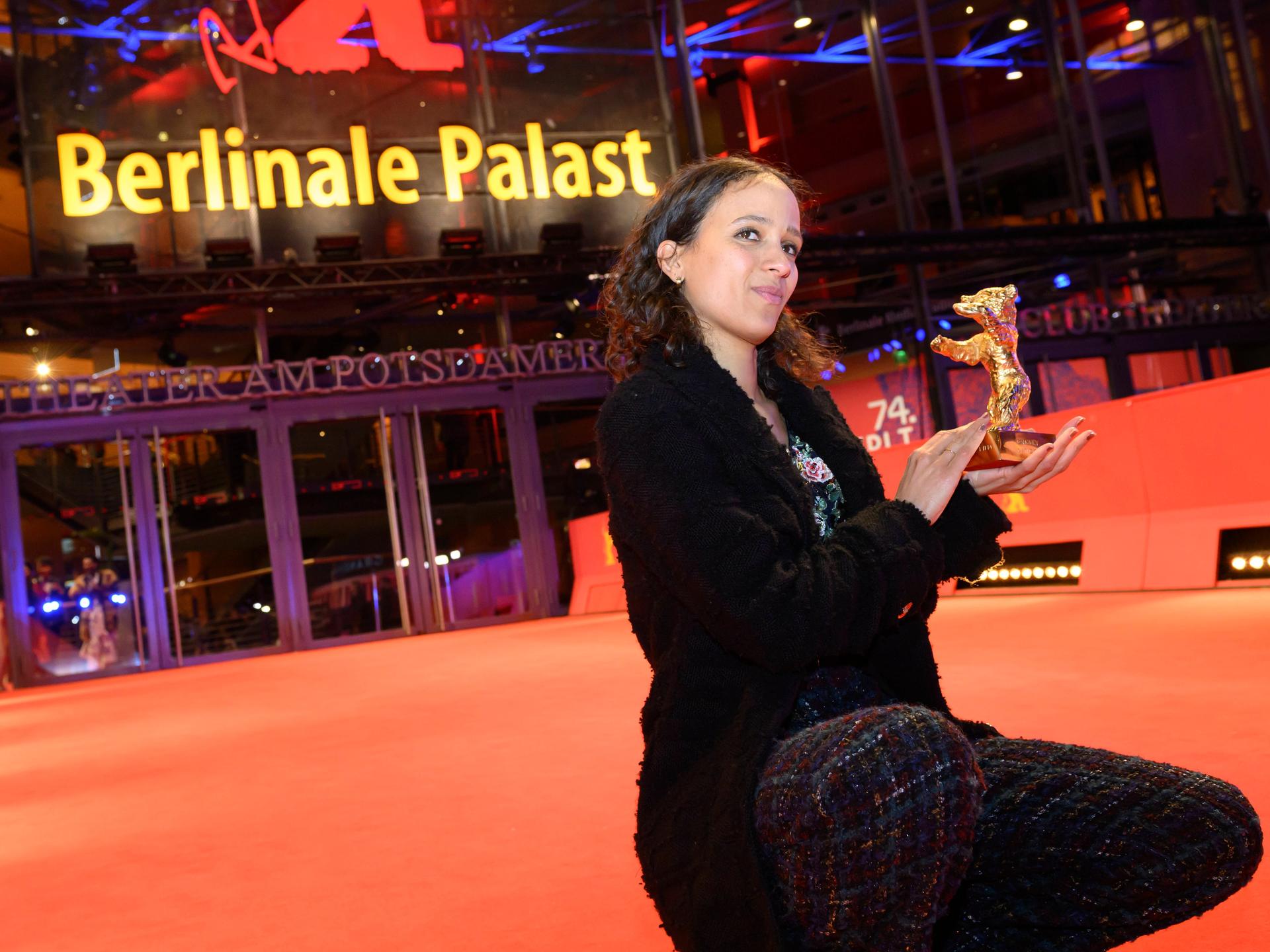 Mati Diop kniet stolz auf dem Roten Teppich vor dem Berlinale-Palast und präsentiert ihren Goldenen Bären, eine handliche Skulptur eines Bären. 