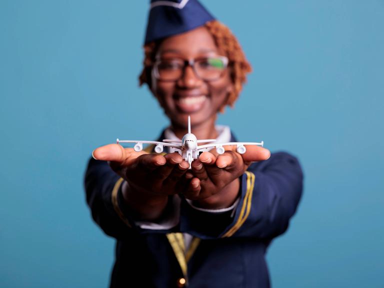 Eine witzige Stewardess hält der Betrachterin einen Mini-Modellflieger entgegen.