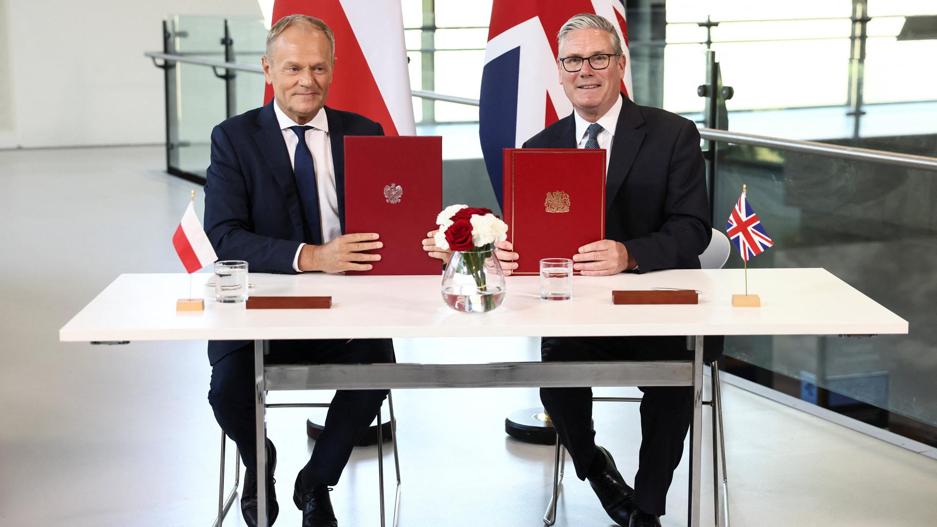 Die beiden Politiker sitzen an einem Tisch und halten die unterzeichneten Dokumente in die Kamera.