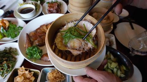 Jemand serviert eine gedämpfte Jakobsmuschel in ihrer Schale mit Glasnudeln, Knoblauch und Lauchzwiebeln in einem chinesischen Restaurant. 