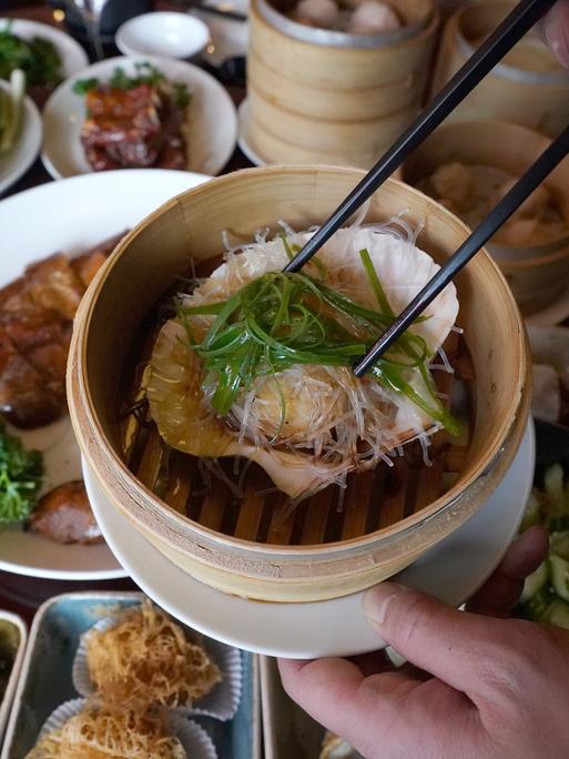 Jemand serviert eine gedämpfte Jakobsmuschel in ihrer Schale mit Glasnudeln, Knoblauch und Lauchzwiebeln in einem chinesischen Restaurant. 