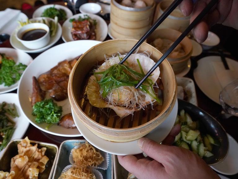 Jemand serviert eine gedämpfte Jakobsmuschel in ihrer Schale mit Glasnudeln, Knoblauch und Lauchzwiebeln in einem chinesischen Restaurant. 