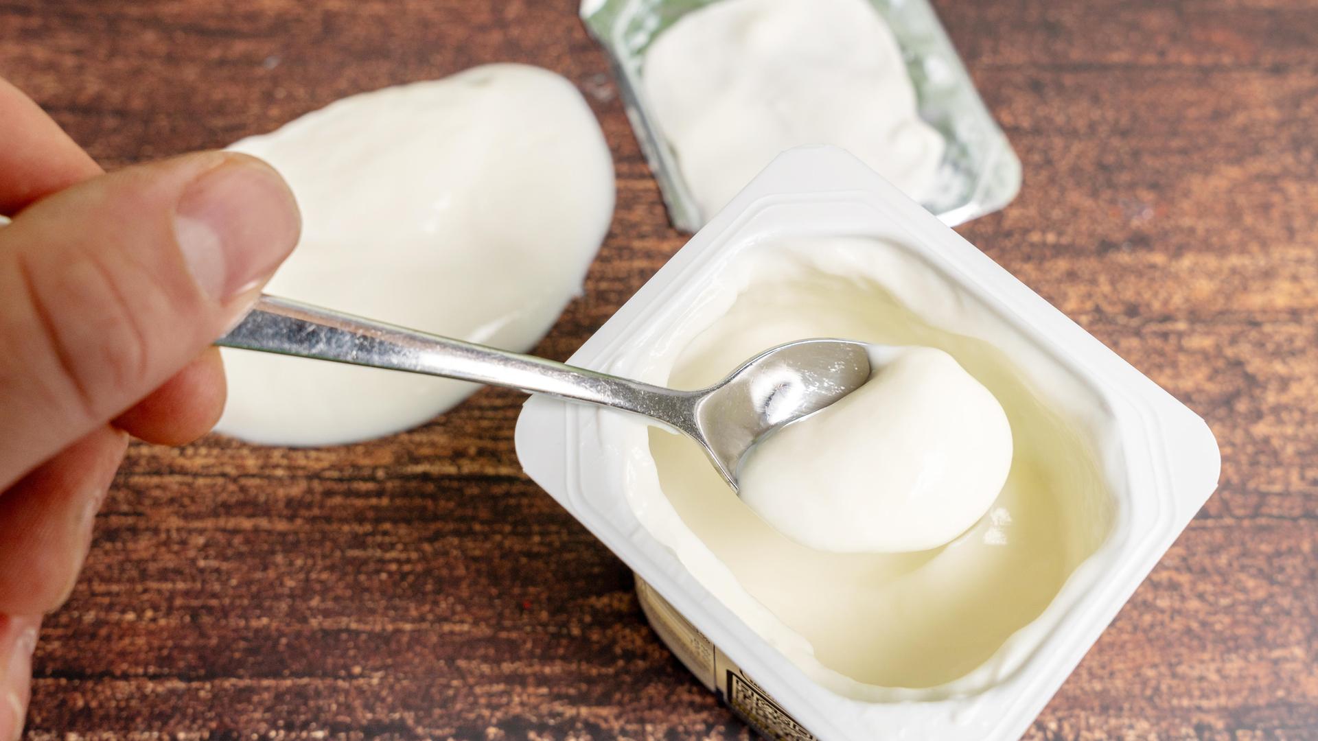 Eine Hand nimmt einen Löffel Naturjoghurt aus dem Joghurtbecher.