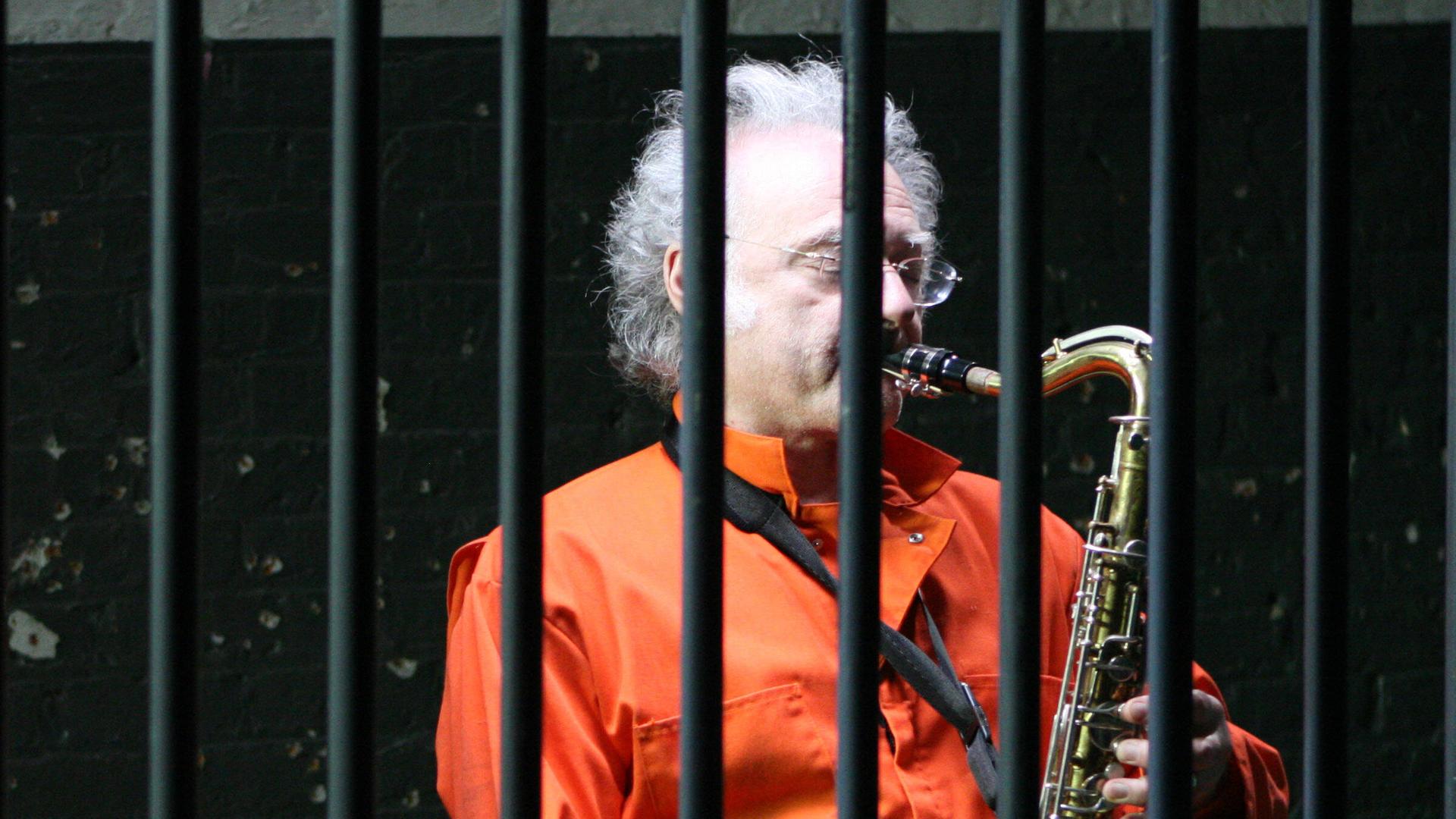 Ein Gefangener spielt hinter Gittern Saxophon.