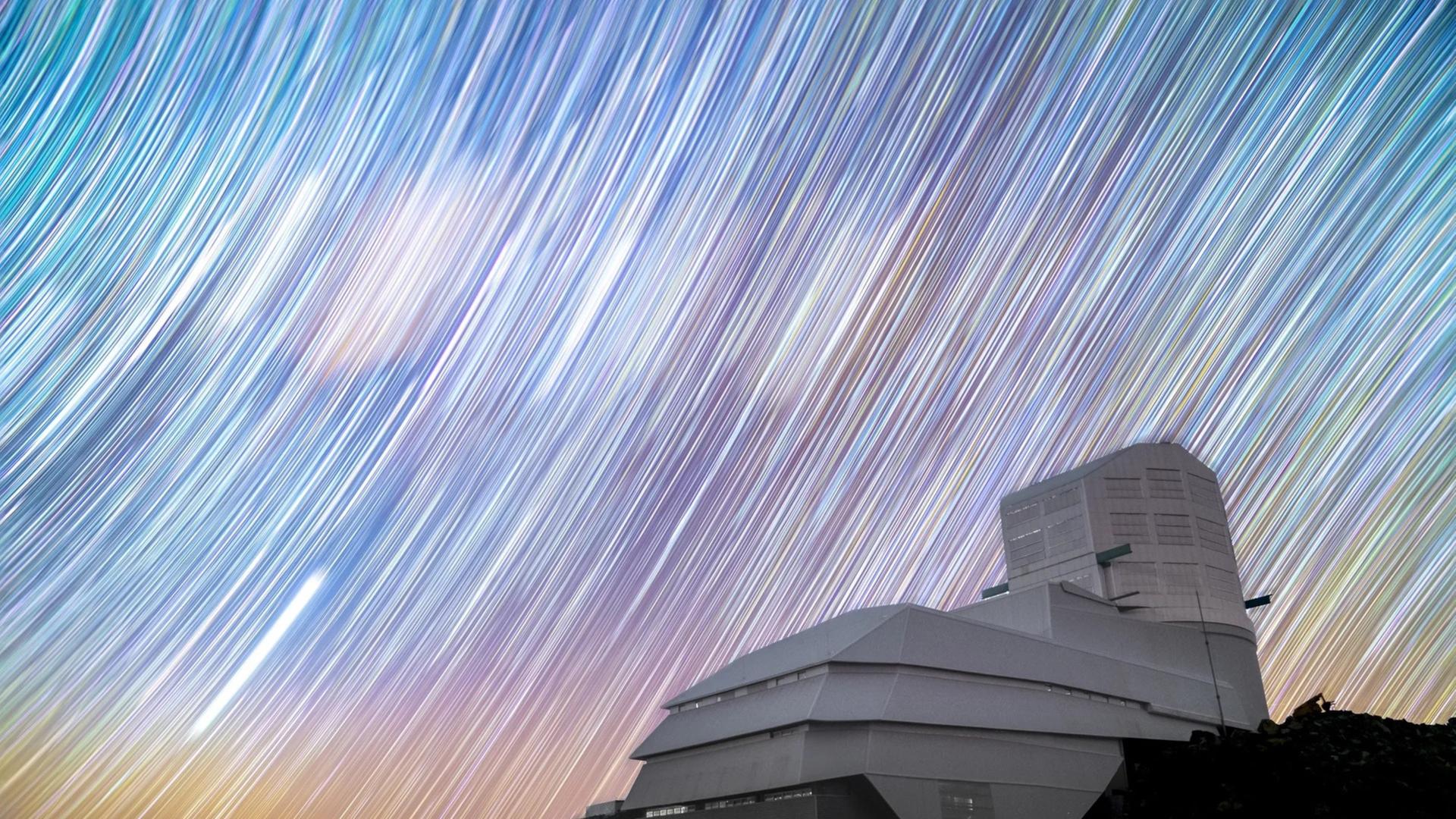Über einem grauen und kastigem Bau sind helle Streifen auf einem mehrfarbigem Himmel zusehen