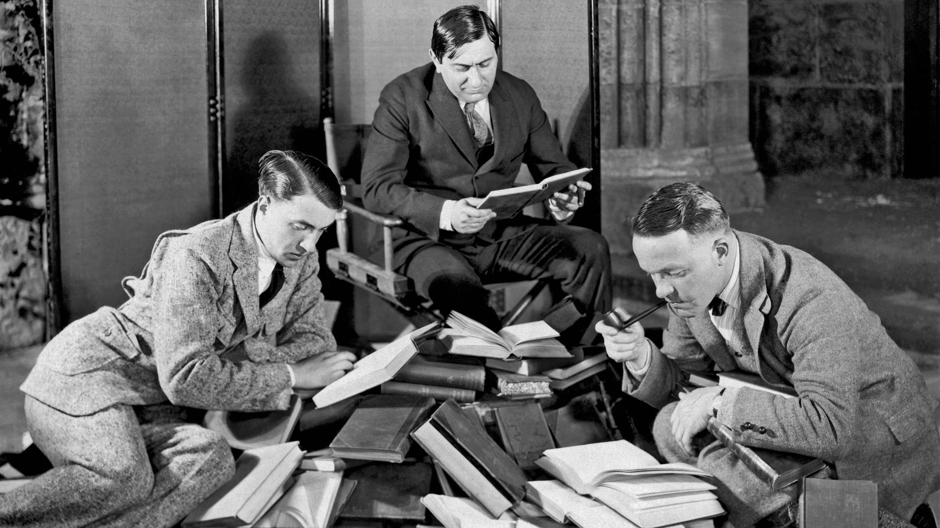 Ernst Lubitsch und zwei andere Männer lesend mit einem Haufen von Büchern