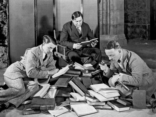 Ernst Lubitsch und zwei andere Männer lesend mit einem Haufen von Büchern